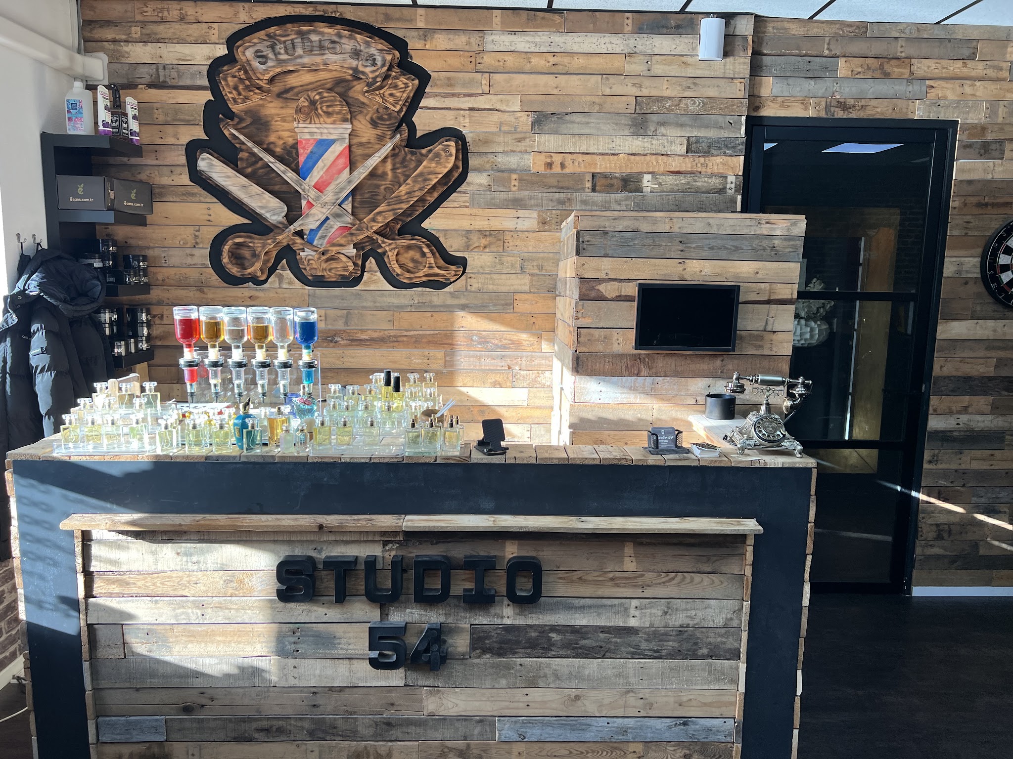 De balie van Studio 54 met de letters STUDIO 54, voor een wand van oud hout met het embleem van schaar, mes en kapperspaal