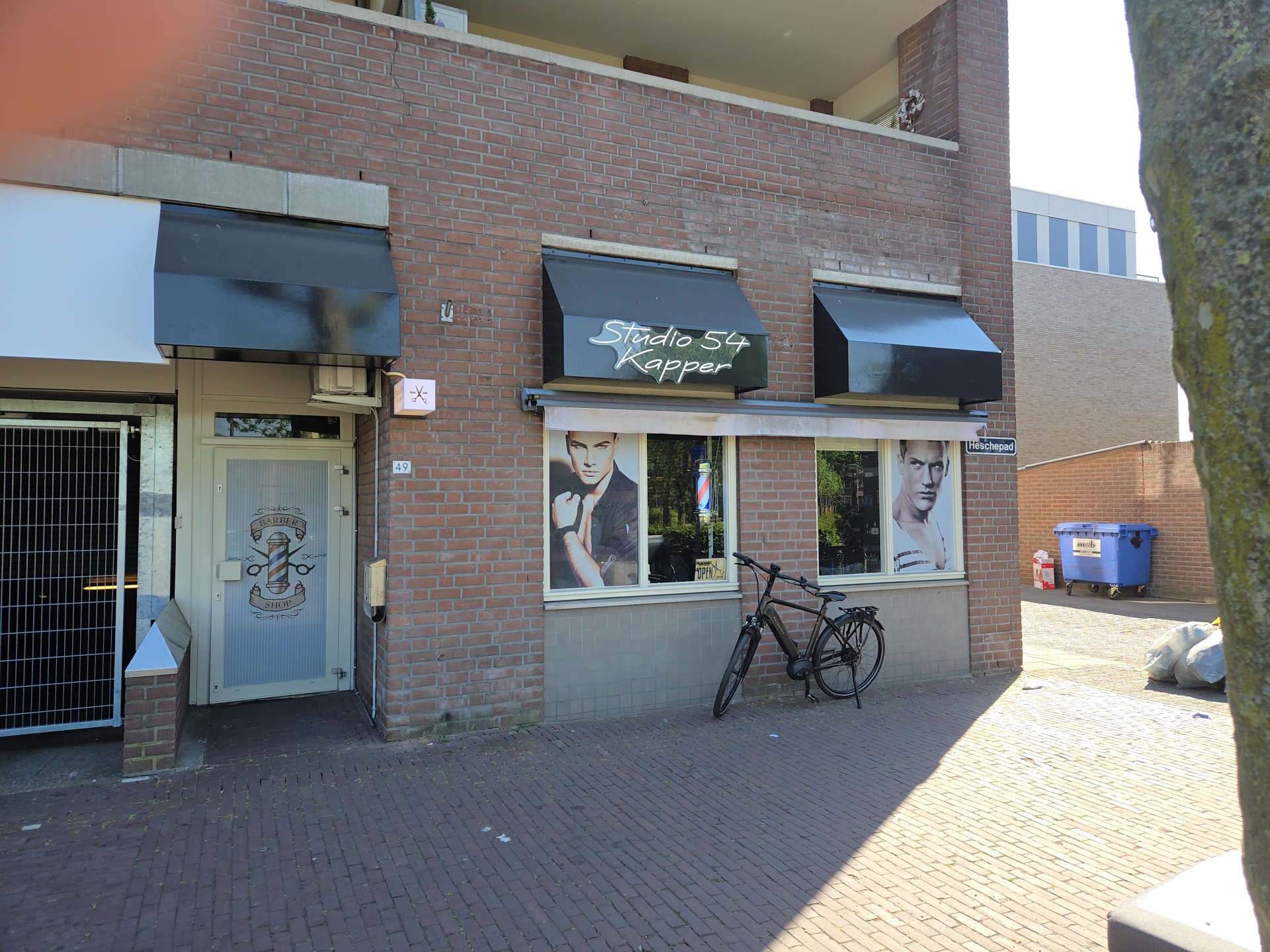 De gevel van Studio 54 aan het Heschepad: bakstenen pui, zwarte luifels en de deur met de baardman-sticker