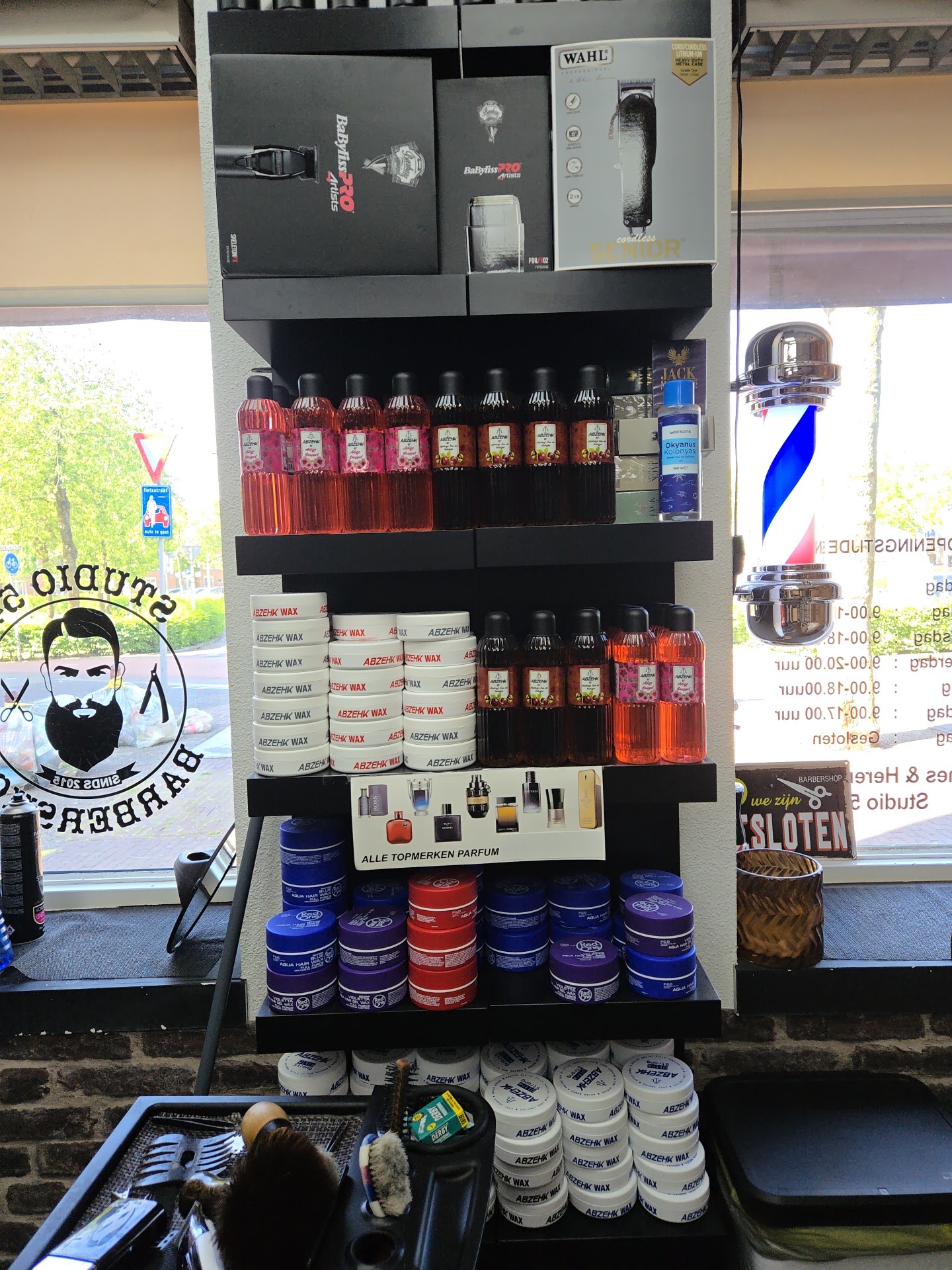 Schappen met haarproducten en een draaiende kapperspaal voor het raam, met de baardman-sticker van Studio 54 op de ruit
